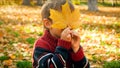 Portrait of cute little boy looking through yellow mapple tree leaf at autumn park