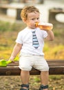 A portrait of cute little boy Sitting on a park bench and sucking from a bottle with a pacifier at summer day Royalty Free Stock Photo