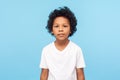 Portrait of cute little boy with stylish curly hairdo in white T-shirt standing, looking at camera with serious attentive face