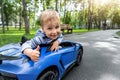 Portrait of cute little caucasain blond toddler boy enjoy having fun riding electric powered toy car by asphalt path Royalty Free Stock Photo