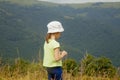 Portrait of cute little child girl in the grass against mountain background. Happy child have a rest in mountains
