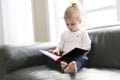 Portrait of Cute little child girl sitting on sofa in living room enjoy reading a big book Royalty Free Stock Photo