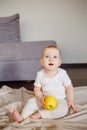 Portrait of a cute little child with one yellow apple, sitting on the floor. Baby girl 9 month old holding a fruit