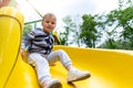 Portrait of cute little cute caucasain blond toddler boy enjoy having fun sliding down modern plastic slide at outdoors Royalty Free Stock Photo