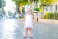 Portrait of cute little emotional blondy toddler girl in white dress playing and catching soap bubbles during walk in the city par