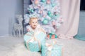 Portrait of a cute little european blond princess girl with a crown in a beautiful dress opening gifts in a studio decorated in Royalty Free Stock Photo