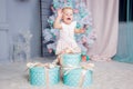 Portrait of a cute little european blond princess girl with a crown in a beautiful dress opening gifts in a studio decorated in Royalty Free Stock Photo