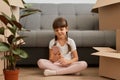 Portrait of cute little girl with braids wearing casual style clothing sitting on a floor near sofa and using mobile phone, Royalty Free Stock Photo
