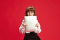 Portrait of cute little girl, child in big glasses, holding tablet against red studio background. Online school lessons Royalty Free Stock Photo