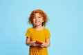 Portrait of cute little girl, child with curly red hair playing on phone, smiling isolated over blue background Royalty Free Stock Photo