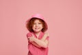 Portrait of cute little girl, child with curly red hair posing in panama and smiling isolated over pink background Royalty Free Stock Photo