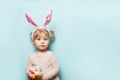 Portrait of a cute little girl dressed in Easter bunny ears holding colorful eggs on blue background Royalty Free Stock Photo