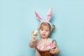 Portrait of a cute little girl dressed in Easter bunny ears holding colorful eggs on blue background Royalty Free Stock Photo