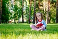 Portrait of Cute Little Girl in Glasses Sitting On Grass With Book In Park Royalty Free Stock Photo