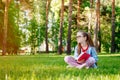 Portrait of Cute Little Girl in Glasses Sitting On Grass With Book In Park Royalty Free Stock Photo