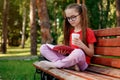 Portrait of Cute Little Girl In Glasses Sitting On The Wooden Bench With Paper Cup Of Cacao And Open Book In Her Hands Royalty Free Stock Photo