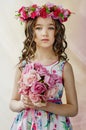 Portrait of cute little girl in nice spring dress, with flowery wreath on head, holds bouquet of flowers. Royalty Free Stock Photo