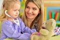 Portrait of cute little girl playing nurse, inspecting teddy bear with stethoscope
