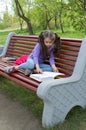 Portrait of cute little girl reading a book sitting on the wooden bench in spring city park Royalty Free Stock Photo