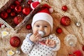 Portrait of cute little girl in Santa Claus red hat with pacifier on a beige plaid with red and white Christmas decorations. Royalty Free Stock Photo