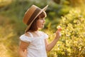 Portrait of cute little girl is smelling wild flower and walks in the rays of a sunset in a flowering meadow, enjoying Royalty Free Stock Photo