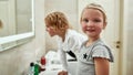 Portrait of cute little girl smiling at camera while washing her face, brushing teeth together with her sibling brother Royalty Free Stock Photo
