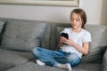 Portrait of cute little girl talking on video call by mobile phone in living room sitting on cozy sofa. Royalty Free Stock Photo