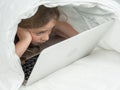 Portrait of a cute little girl using a laptop while lying under a blanket. Royalty Free Stock Photo