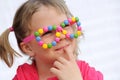 Portrait of cute little girl wearing funny glasses, decorated with colorful smarties, candies