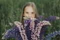 Portrait of a cute little happy seven year old kid girl with bouquet of bloom flowers lupines in a field in nature outdoor. Royalty Free Stock Photo