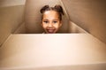 Portrait of a cute little hispanic girl playing with a cardboard box in a new apartment. Cute mixed race girl hiding in Royalty Free Stock Photo