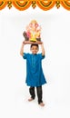 Portrait of cute little Indian boy holding a Ganesh idol or lord ganesha or ganapati murti /statue over his head, taking home on G