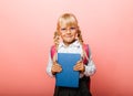 Portrait of a cute little kid girl on a pink background. Child schoolgirl looking at the camera, holding a book and straightens Royalty Free Stock Photo