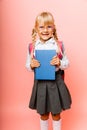 Portrait of a cute little kid girl on a pink background. Child schoolgirl looking at the camera, holding a book and straightens Royalty Free Stock Photo