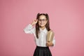 Portrait of cute little kid girl on pink background. Schoolgirl looking at camera, holding book and straightens glasses Royalty Free Stock Photo