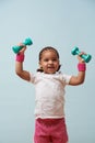Portrait of cute little mulatto girl lifting dumbbells. Pale blue background