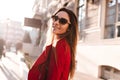 Portrait of cute long-haired girl in sunglasses looking over shoulder on blur city background. Outdoor photo of joyful