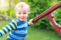 Portrait of cute mischievous caucasian blond baby boy holding wooden banister climbing staircase at outdoor backyard playground. Royalty Free Stock Photo