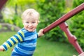 Portrait of cute mischievous caucasian blond baby boy holding wooden banister climbing staircase at outdoor backyard playground.