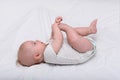 Portrait of a cute 3 months baby lying on bed. Newborn lies on his back and played foot