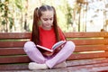 Portrait of Cute Pensive Little Girl Sitting On The Wooden Bench In Park With Open Book in Her Hands Outdoors Royalty Free Stock Photo