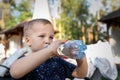 Portrait of cute playful little caucasian blond thirsty toddler boy kid holding plastic bottle and drinking water on hot Royalty Free Stock Photo