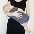 Portrait of cute plump cherubic baby infant toddler in grey bodysuit holded by mother in black dress eating breast milk.