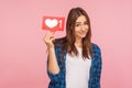 Portrait of cute positive girl in checkered shirt smiling playfully and holding social media like icon Royalty Free Stock Photo