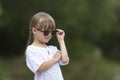 Portrait of cute pretty funny young girl with blond braids in white dress and dark sunglasses. Royalty Free Stock Photo