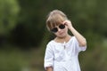 Portrait of cute pretty funny young girl with blond braids in white dress and dark sunglasses. Royalty Free Stock Photo