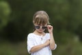 Portrait of cute pretty funny young girl with blond braids in white dress and dark sunglasses. Royalty Free Stock Photo