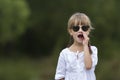 Portrait of cute pretty funny young girl with blond braids in white dress and dark sunglasses. Royalty Free Stock Photo