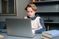 Portrait of cute pupil boy using typing laptop computer doing online lesson via Internet at desk, selective focus. Royalty Free Stock Photo