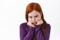 Portrait Of Cute Redhead Girl Pouting, Making Coy Sulking Face And Look Gloomy From Under Forehead, Standing Upset